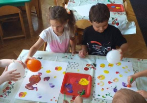 Na zdjęicu widać grupkę dzieci, które stemplują balonami maczanymi w farbie.